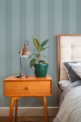 Self-adhesive Chevron wallpaper with a subtle zigzag pattern in varying shades of light and dark greens, applied to a bedroom wall behind a wooden nightstand with a potted plant and a metal desk lamp.