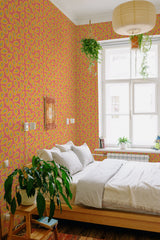 A room with vibrant yellow lemons and green leaves on a pink background covers the walls, creating a lively and playful vibe. The pattern is repeated across the entire wall, with white wooden window frames allowing natural light into the space. The room is cozy with a bed, woven wall art, and various potted plants adding to the warmth. The wallpaper design brings a fresh, nature-inspired element to the traditional wallpaper.