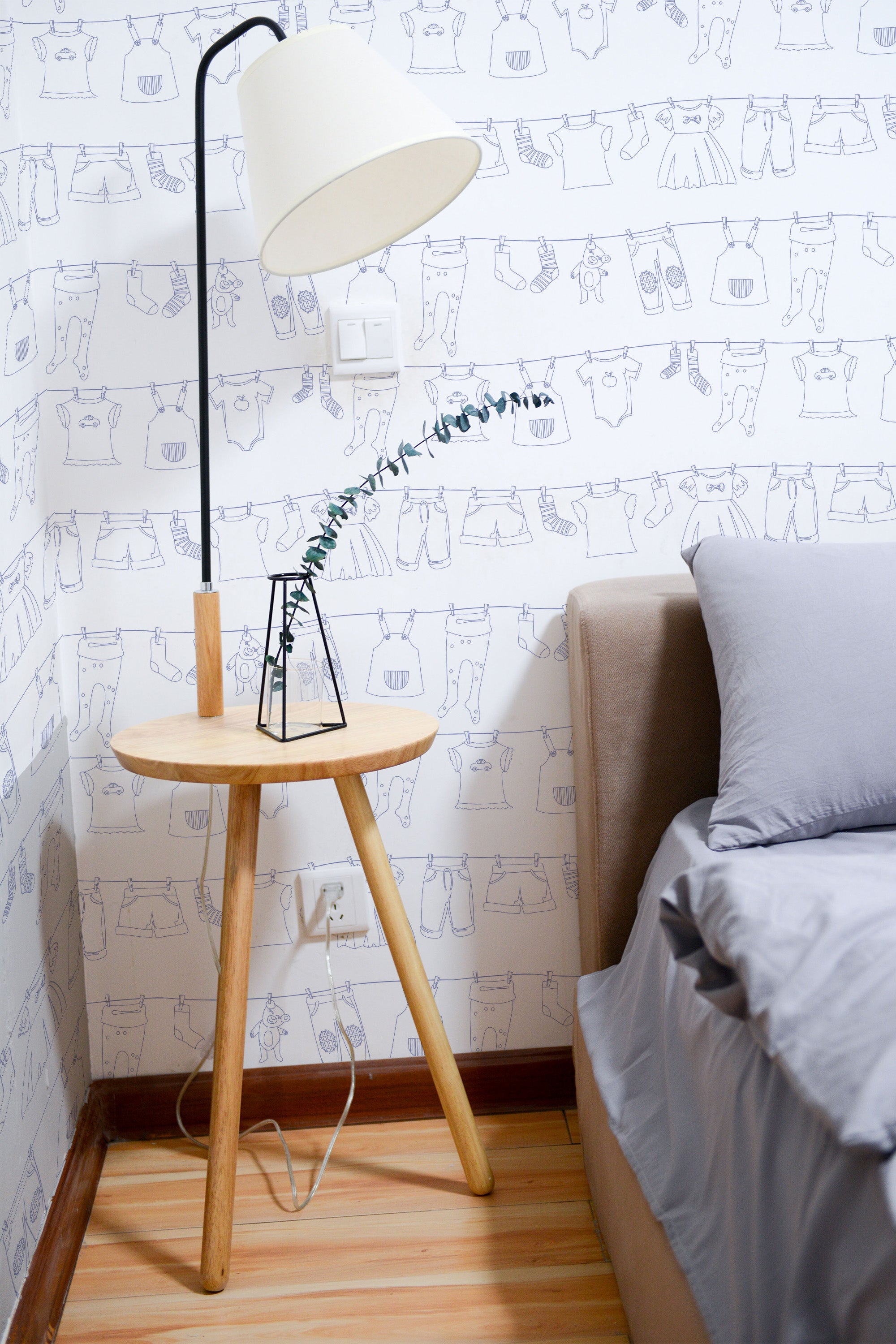 Self-adhesive wallpaper with a playful laundry-themed design, featuring line drawings of clothing items like shirts, pants, and socks on hangers and clotheslines. The pattern adds a whimsical touch to the room's decor.