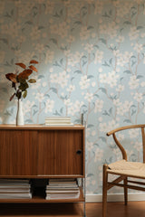 Self-adhesive wallpaper with a delicate blossoming tree design on a soft pastel blue background, featuring branches adorned with white and pink flowers and muted green leaves.