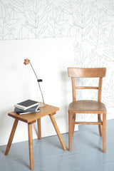 Self-adhesive wallpaper with a delicate big floral design in light green outlines on a white background, adorning a room with minimalistic wooden furniture.