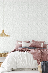 Room with large floral print wallpaper in soft, muted tones, complementing a cozy bed with pink and gray linens. Traditional wallpaper.