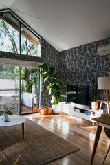 Self-adhesive black brush stroke wallpaper with an abstract linear pattern covering the walls of a modern living room, creating a bold and artistic backdrop.