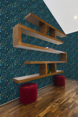 A room with dark blue wallpaper adorned with vibrant, intricate floral patterns, evoking a lush meadow. The design includes small flowers, leaves, and delicate stems spread uniformly across the wall, creating a warm and inviting ambiance. The wallpaper is complemented by wooden floating shelves and rich wood flooring, adding a cozy and rustic vibe to the space. Traditional wallpaper.