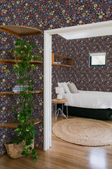 A room adorned with wallpaper covered in a pattern of small, colorful floral designs against a dark background, adding a vibrant yet classic touch to the space. The intricate floral motifs are repeated throughout, with hues of pink, yellow, green, and blue, complementing the natural wood accents and simple furnishings in the room. This is traditional wallpaper.