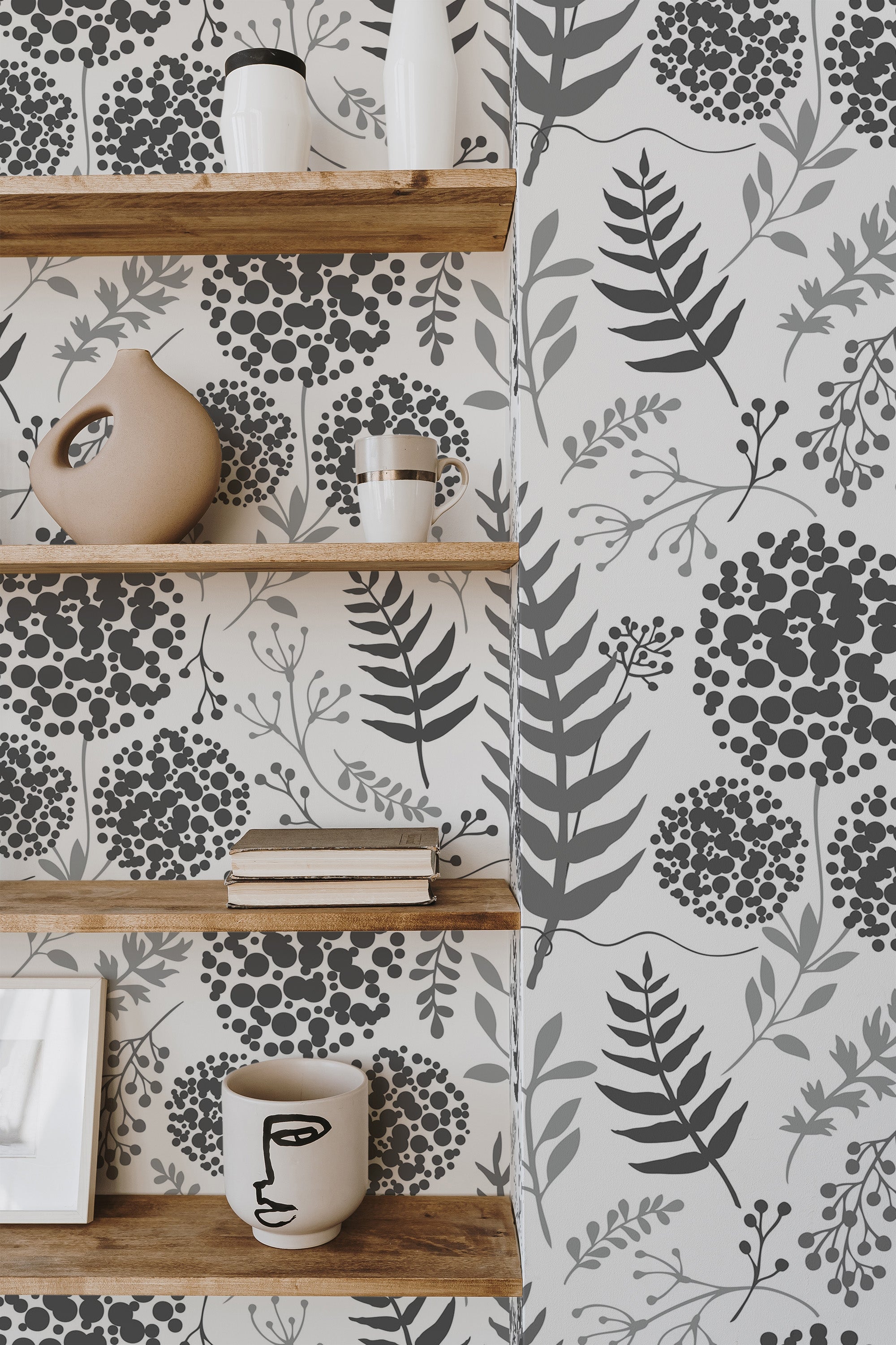 Self-adhesive monochrome floral wallpaper with a pattern of dark grey flowers, leaves, and branches on a light background, complementing wooden shelves and neutral-colored decor in the room.