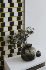 Self-adhesive Geometric optical tile wallpaper with a repeating pattern of black and white tiles arranged in offset rows, accented by thin yellow borders.