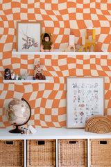 Self-adhesive funky geometric wallpaper with wavy orange and cream checkered patterns creating a dynamic, retro visual effect.