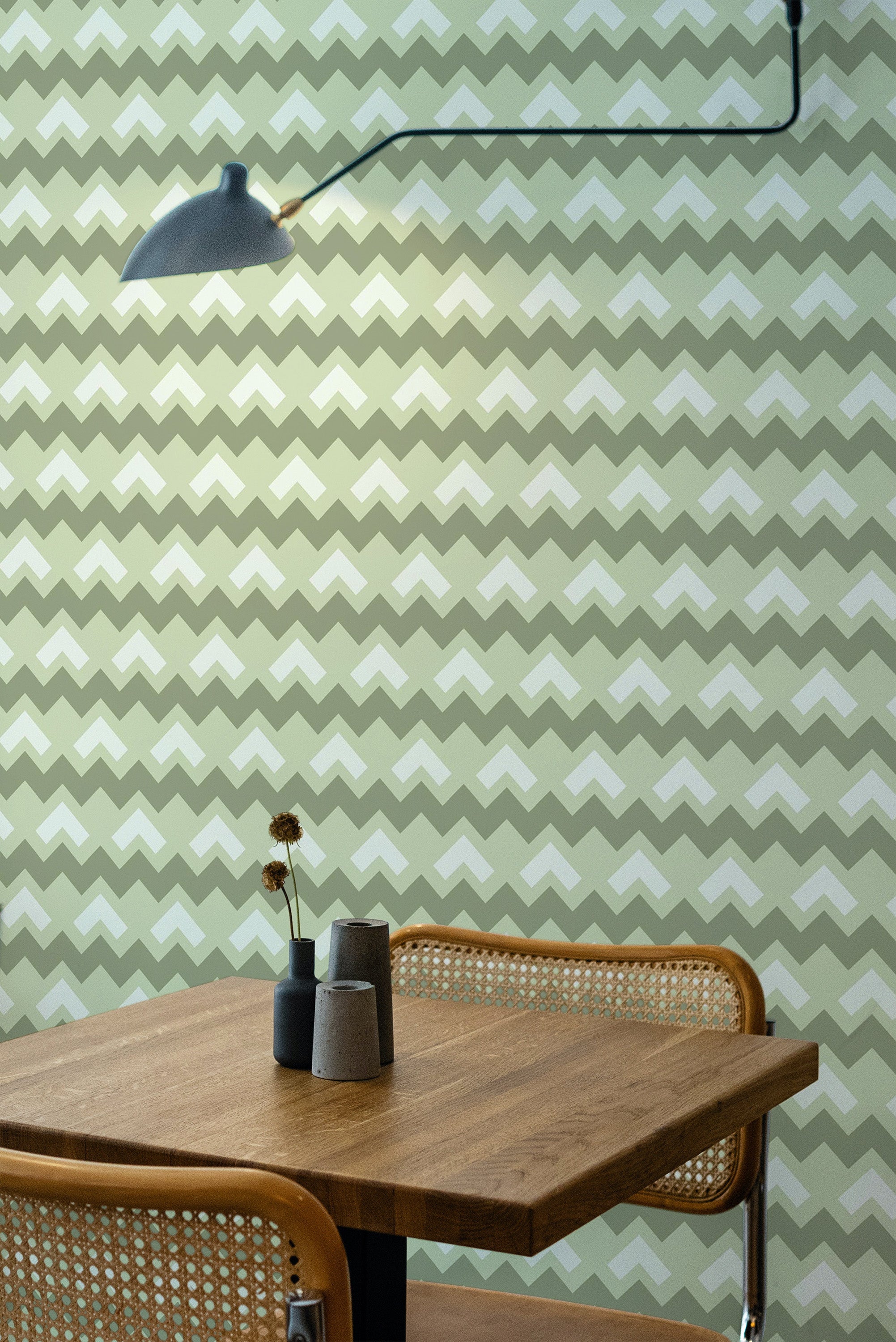Self-adhesive green chevron wallpaper with alternating shades of green and cream, forming a zigzag pattern on the wall behind a wooden table and chairs.