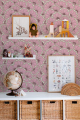 Self-adhesive wallpaper with a bold eclectic print in shades of pink featuring large intricate floral patterns behind white shelves displaying toys, framed art, and a globe.