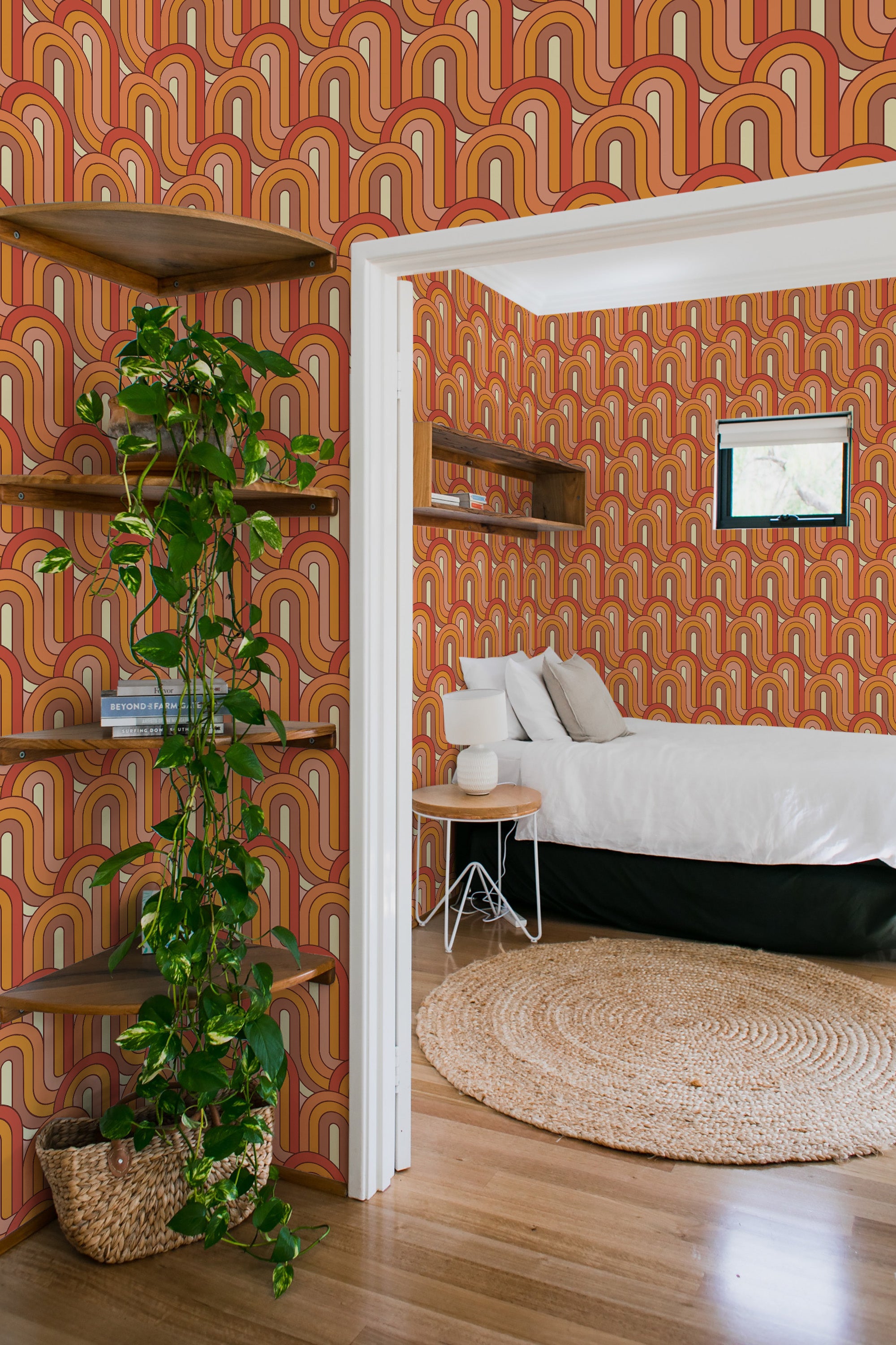 A room with Retro wave designed wallpaper in shades of brown, orange, red, and beige with repetitive arches creating a vibrant and nostalgic atmosphere. The wallpaper complements the warm wooden tones and greenery in the room, combining vintage style with natural elements. Traditional wallpaper.