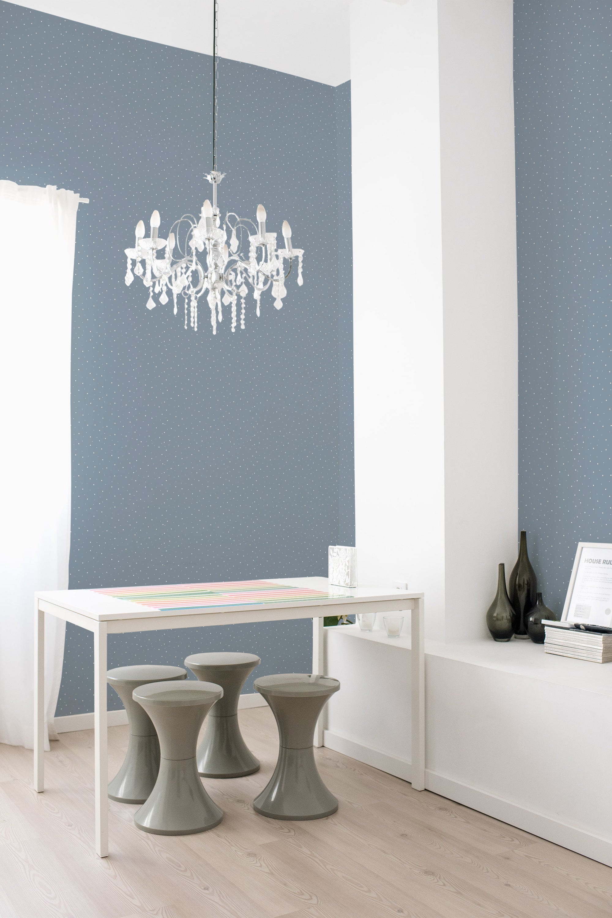 Blue wallpaper with small white polka dots set in a minimalist room with a white table, modern stools, and a chandelier. Traditional wallpaper.