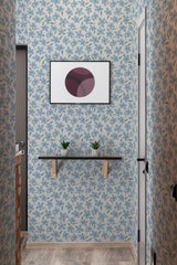 Light blue wallpaper with darker blue and teal floral patterns covering the walls in a hallway. A small shelf with two succulents sits below a modern art print. Traditional wallpaper.