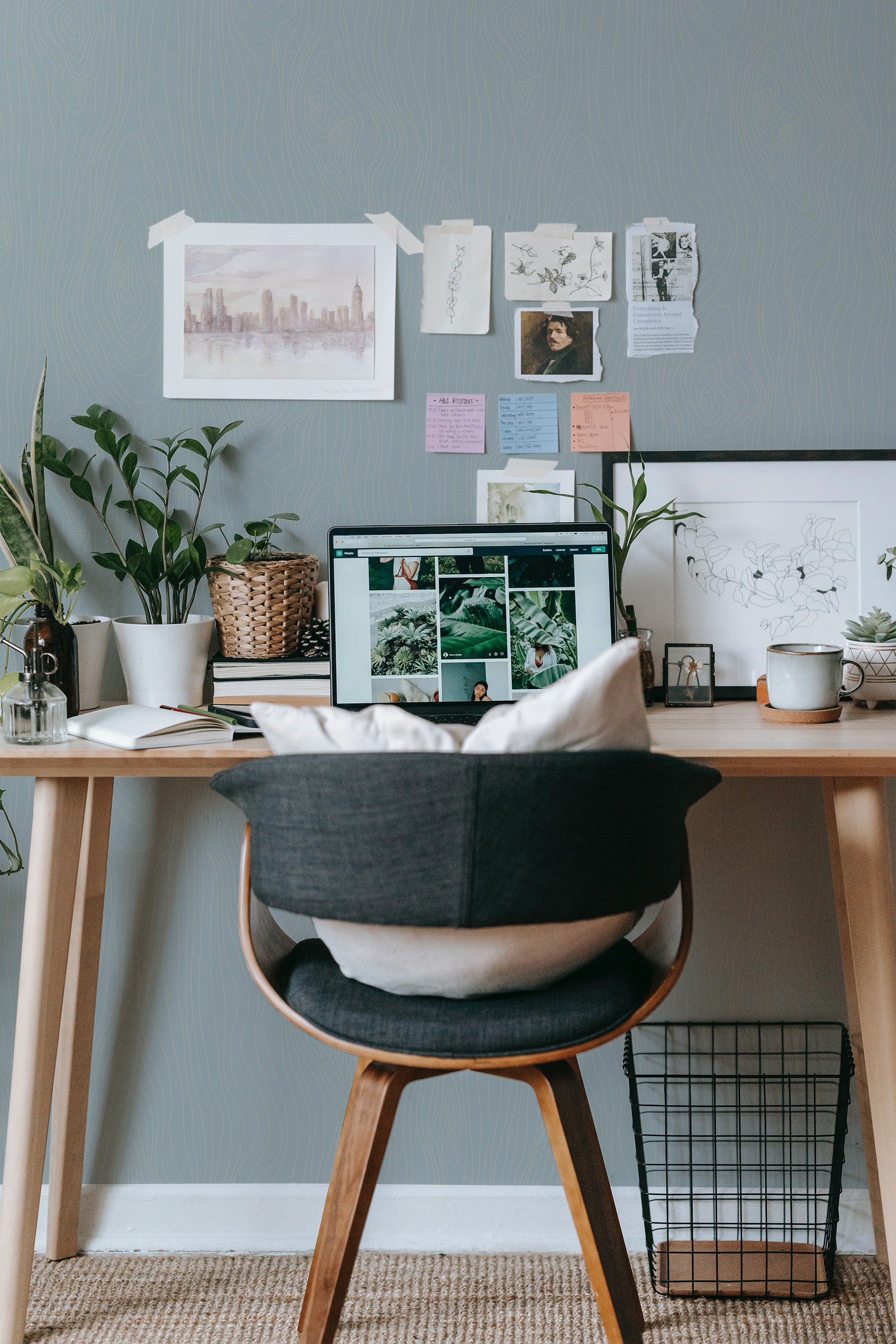 Self-adhesive gray wood wall wallpaper with a faux plank design in a room with a desk, computer, chair, and houseplants.