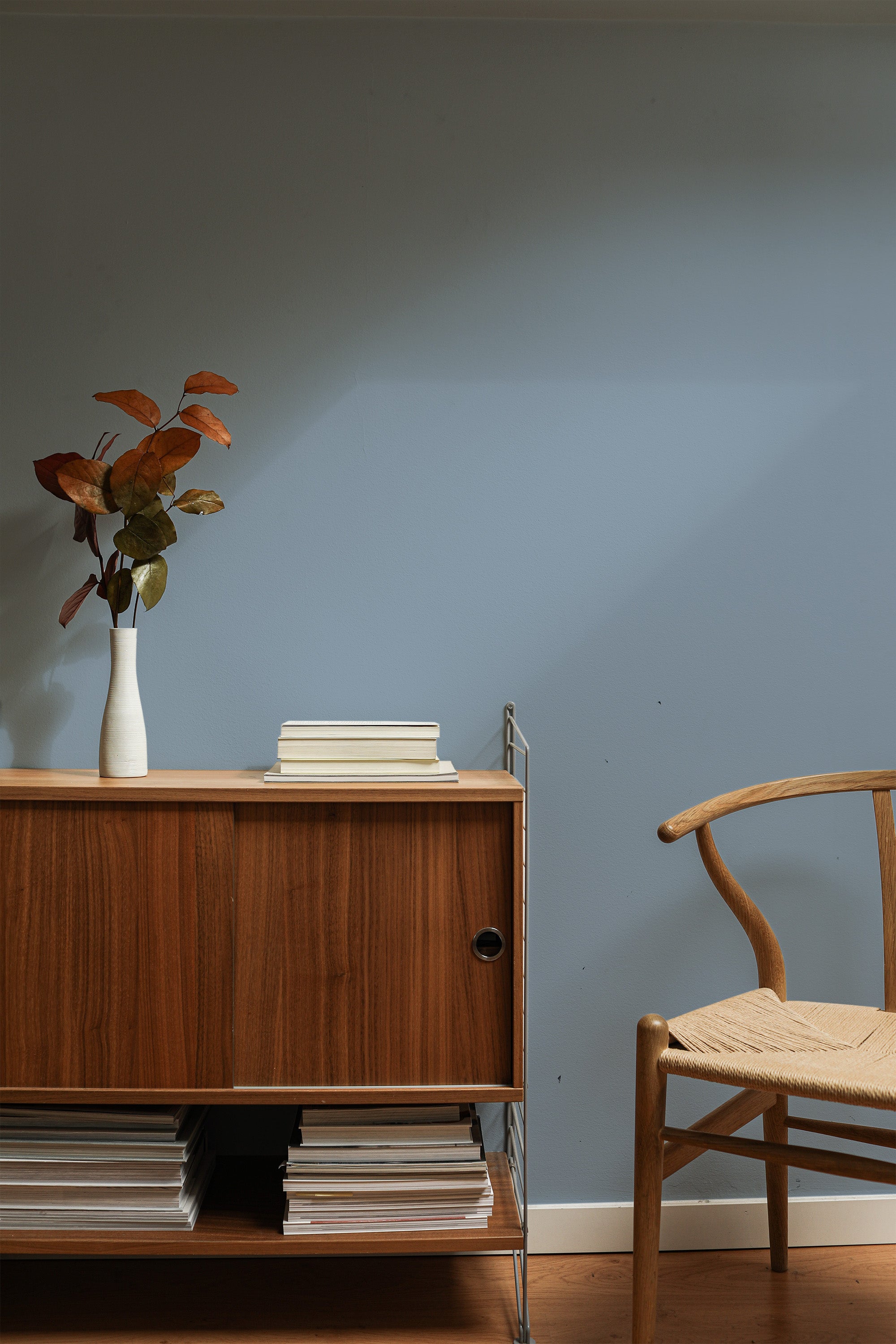 Self-adhesive wallpaper in a dusty blue solid color providing a minimalist and serene backdrop in a room with wooden furniture and decor accents.