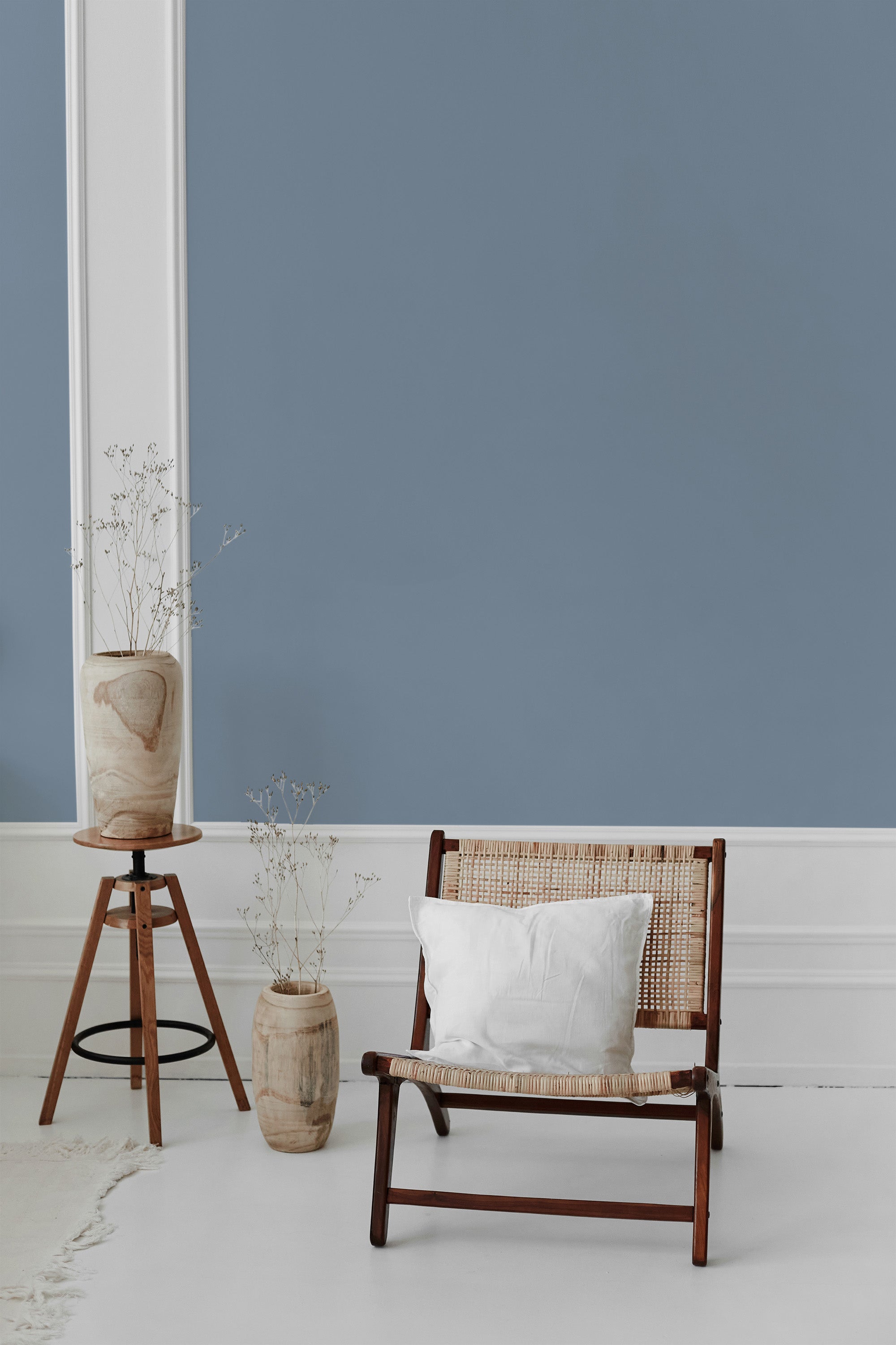 A room with dusty blue solid-colored wallpaper on the wall with white trim accents, complemented by minimalist wooden furniture and decorative vases. Traditional wallpaper.