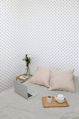 Self-adhesive wallpaper with a design of small purple polka dots evenly spaced on a light background, covering the wall in a room with neutral decor.
