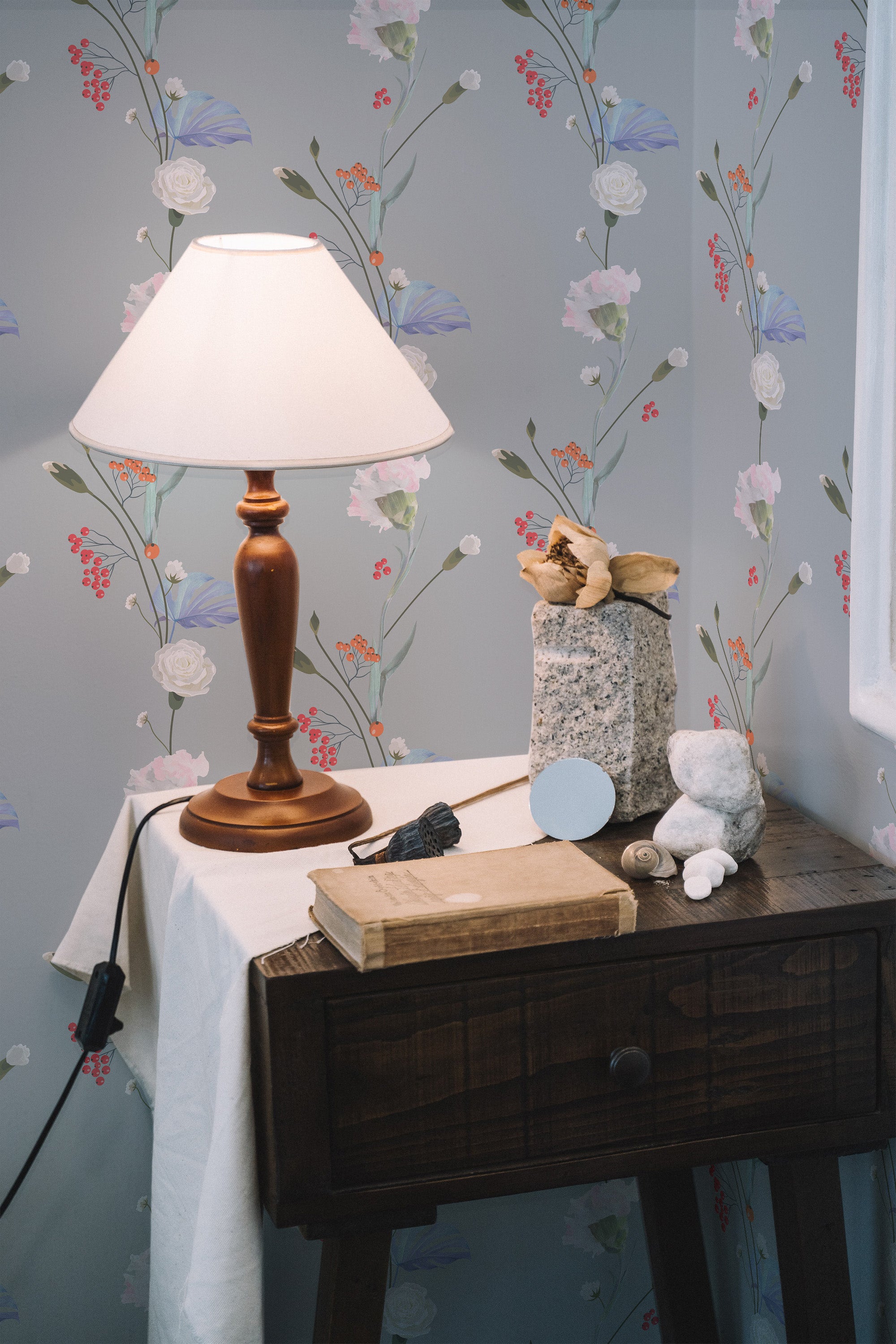 Self-adhesive wallpaper with delicate flower drawings, showcasing thin, vertical stems adorned with white and purple flowers and red berries against a light gray background. The room is warmly lit by a table lamp placed on a wooden side table, adding a cozy ambiance.