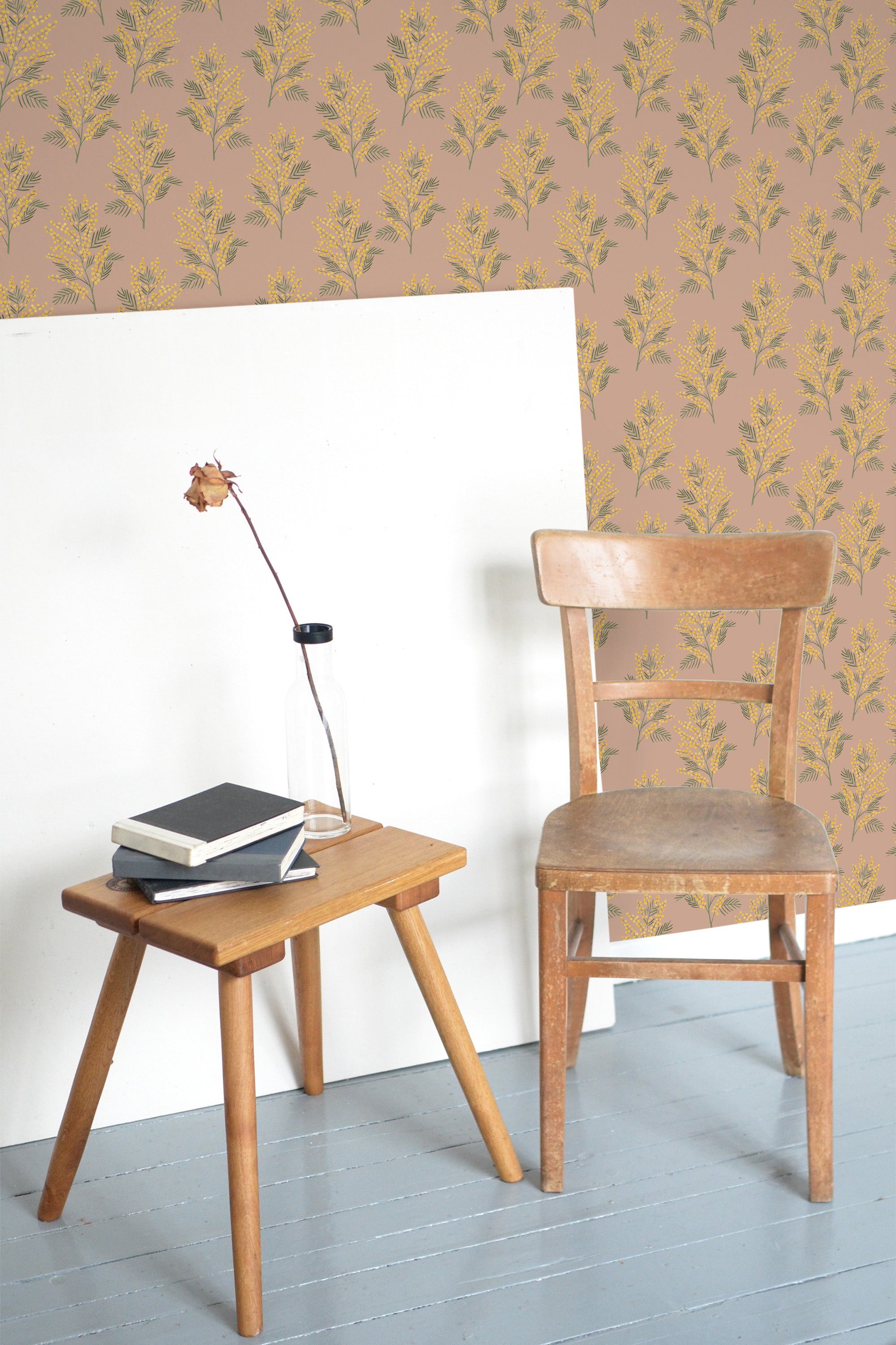 Self-adhesive wallpaper with a pattern of autumnal flowers in warm tones on a room wall, accompanied by a wooden chair and table with books and a lamp.