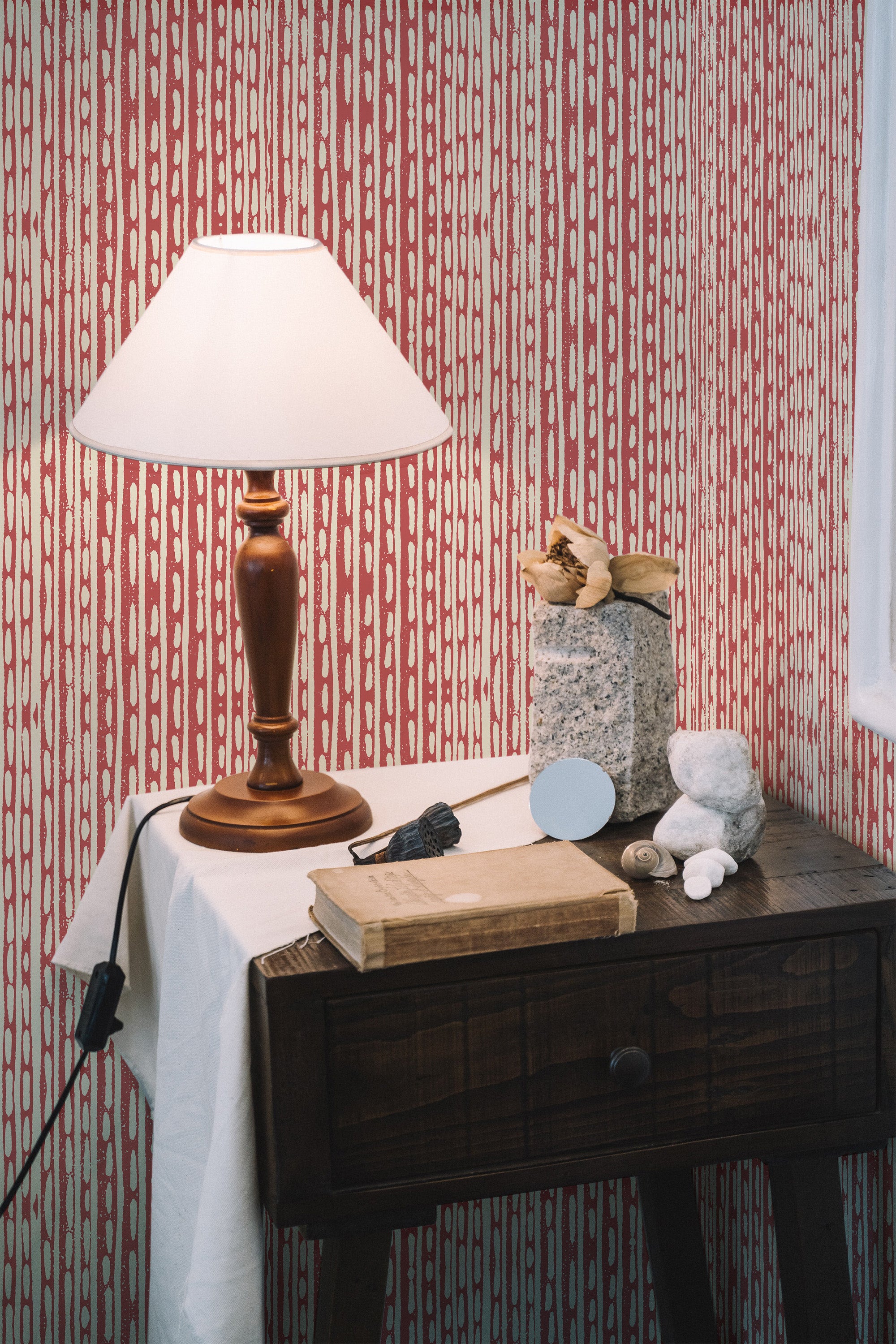 Self-adhesive wallpaper with red and white vertical abstract brush lines on a room wall, accompanied by a wooden table and lamp.