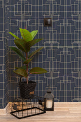 Self-adhesive wallpaper with a Great Gatsby-inspired geometric pattern in gold on a navy blue background, enhancing an elegant room corner with a potted plant and decorative lantern.