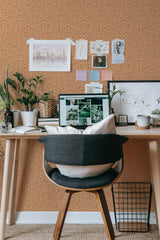 Self-adhesive wallpaper with an autumn branch pattern in warm tones on a home office wall, complemented by a wooden desk and houseplants.