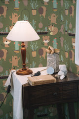 Self-adhesive wallpaper with a playful hedgehog and plant pattern on a green background, accompanied by wooden furniture and a table lamp.