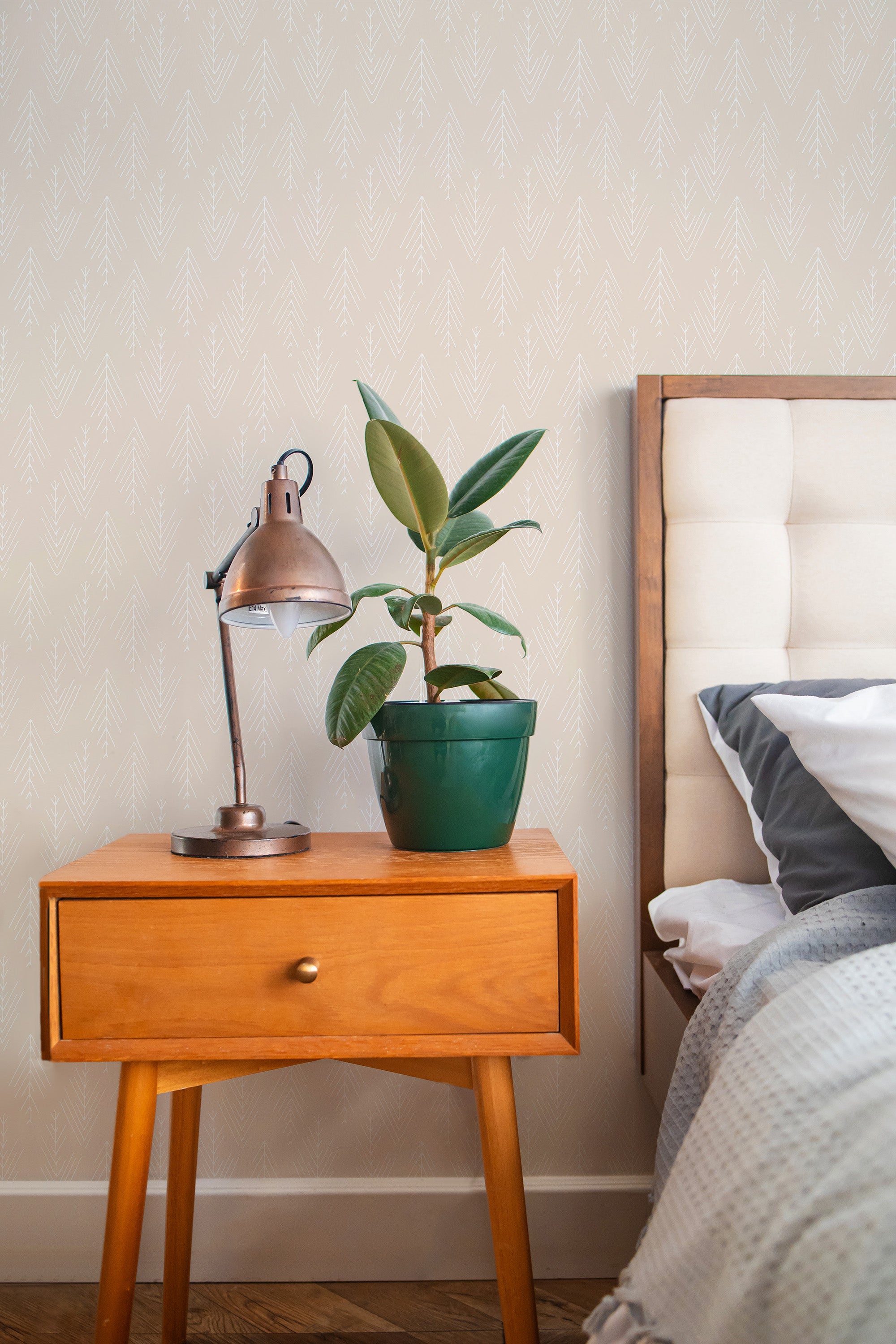Self-adhesive wallpaper with a subtle, neutral hygge pattern on a bedroom wall beside a wooden nightstand with a plant and lamp.