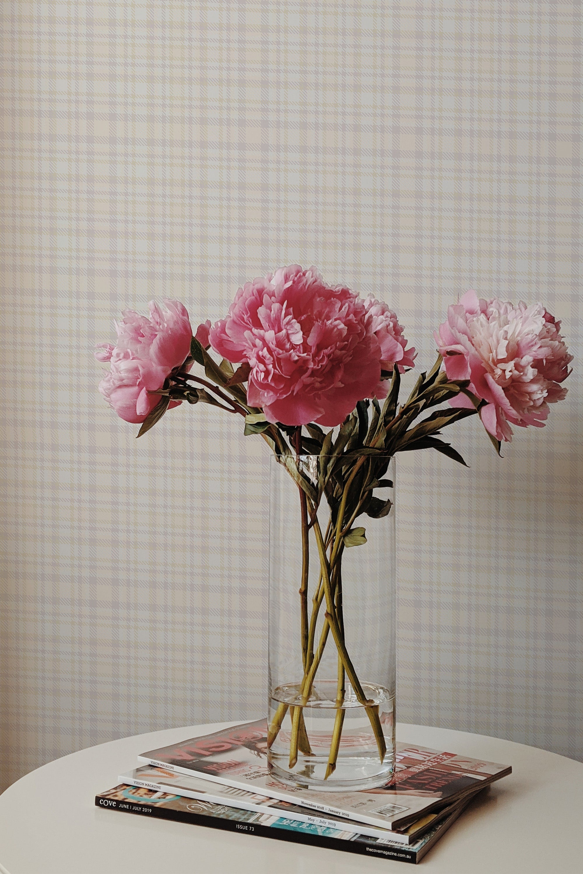 Self-adhesive beige faux tweed wallpaper with subtle plaid pattern in a room, accented by a vase with pink flowers on a table.