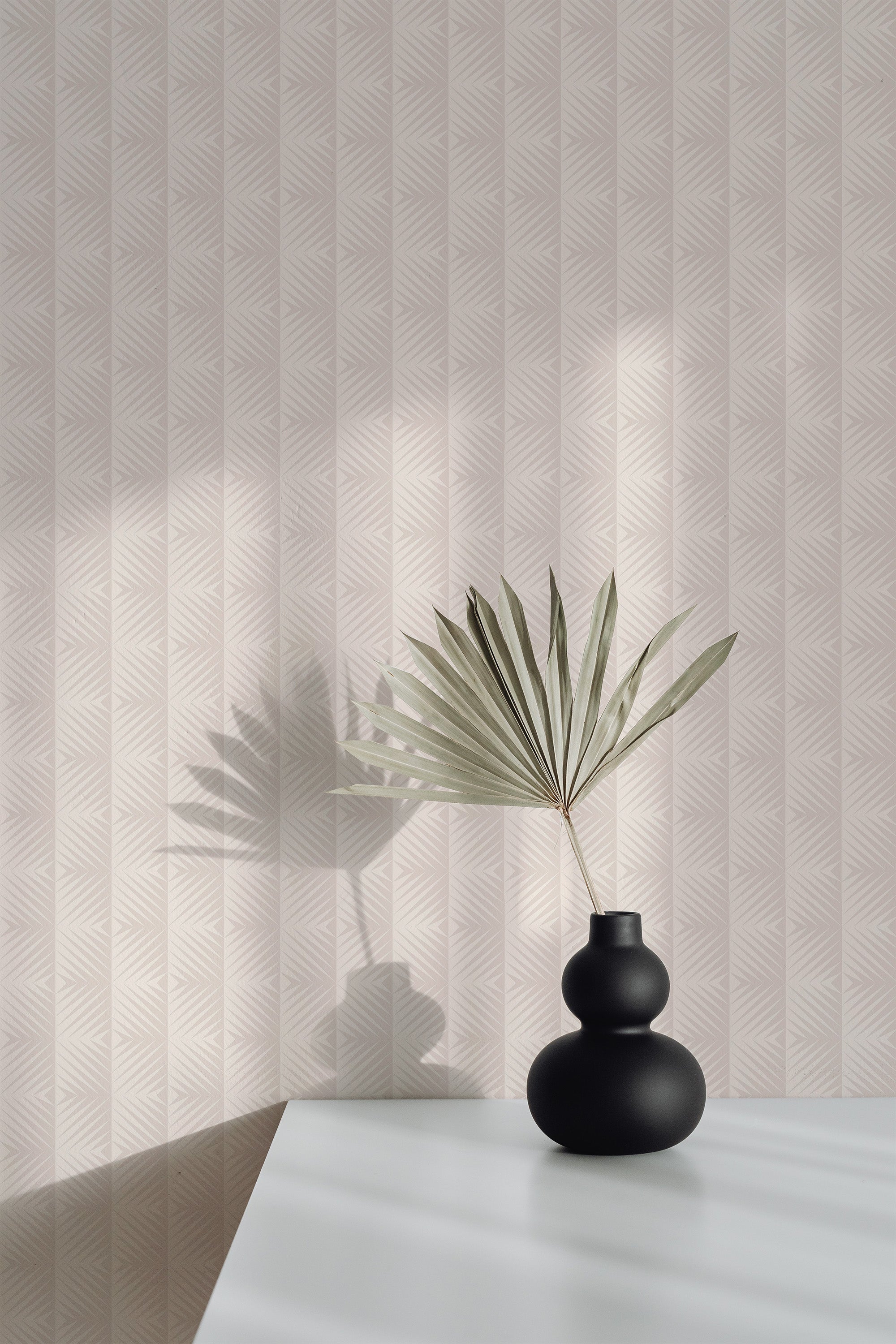 Self-adhesive neutral funky tile wallpaper with a geometric pattern, accompanied by a vase with dried palm leaf on a white surface casting a soft shadow on the wall.