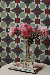 Self-adhesive wallpaper with a geometrical star tile pattern in shades of green, beige, and red with a bouquet of pink peonies in the foreground.