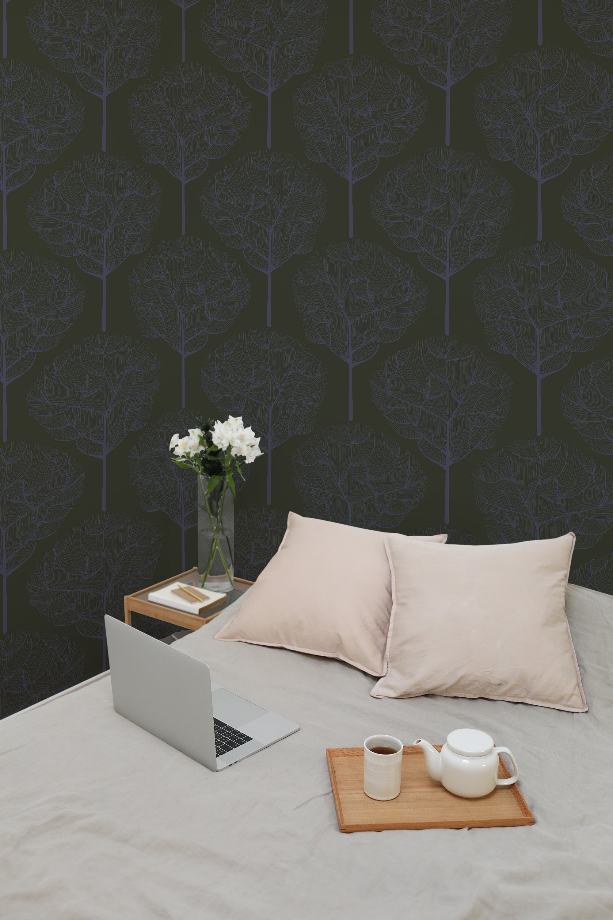 Self-adhesive wallpaper with dark blue oak tree pattern on a room wall, accompanied by a bed with a laptop, pillows, a side table, and a vase of flowers.