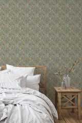 Self-adhesive Sage Meadow wallpaper with a pattern of various plants and flowers in soft green, blue, and pink hues, covering a bedroom wall behind a wooden bed and side table.