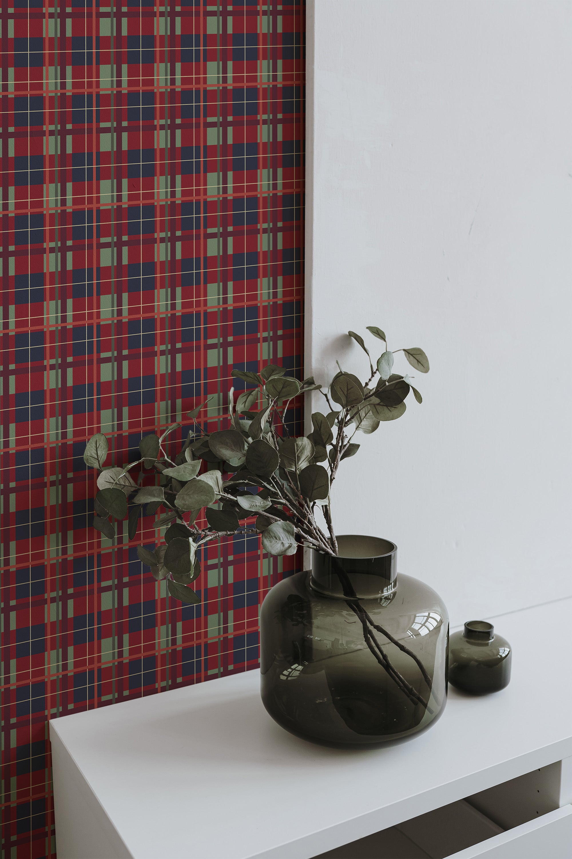 Self-adhesive burgundy plaid wallpaper on a wall with a white shelf holding green vases and foliage.