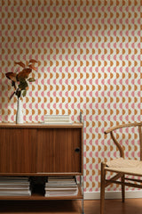 Self-adhesive wallpaper with a mid-century half circles design in peach and cream colors on a wall behind a wooden credenza and chair, complemented by a vase with dried plants.