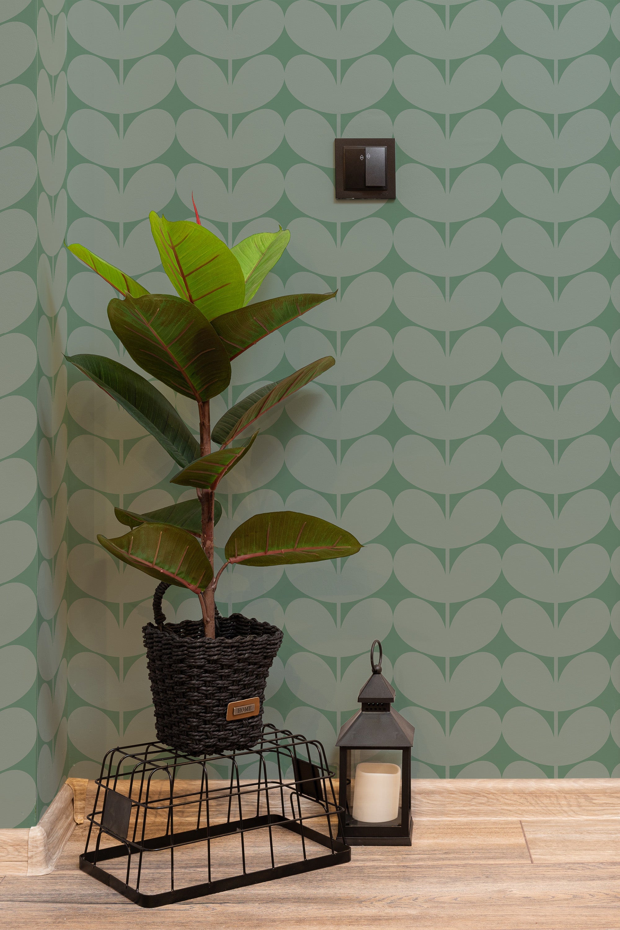 Self-adhesive wallpaper with green leaf patterns on a light background, complemented by a potted plant and a lantern on the floor.