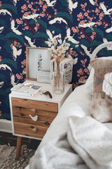 Self-adhesive wallpaper with a bold cranes pattern in blue background, accented with pink flowers and white birds in a furnished room.