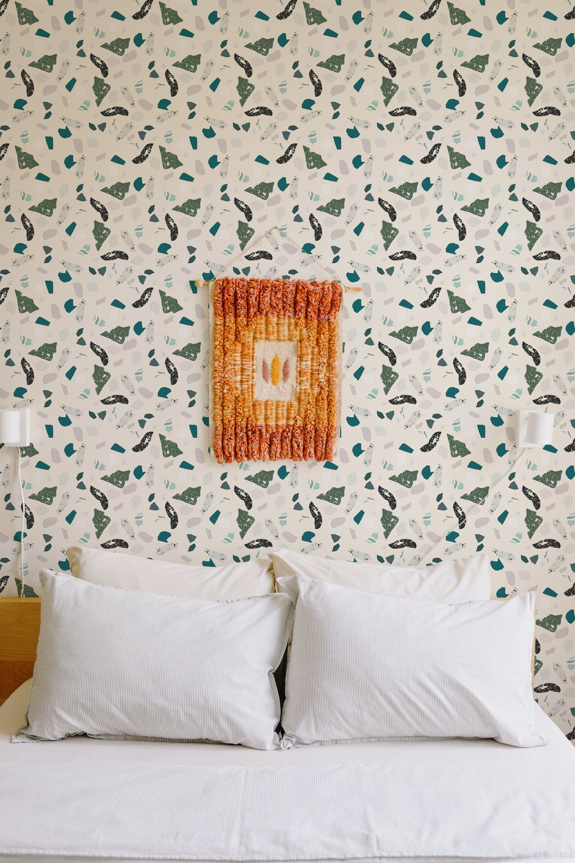 Self-adhesive wallpaper with a green terrazzo pattern of variously shaped fragments on a light background, above a bed with white pillows.