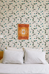 Self-adhesive wallpaper with a green terrazzo pattern of variously shaped fragments on a light background, above a bed with white pillows.