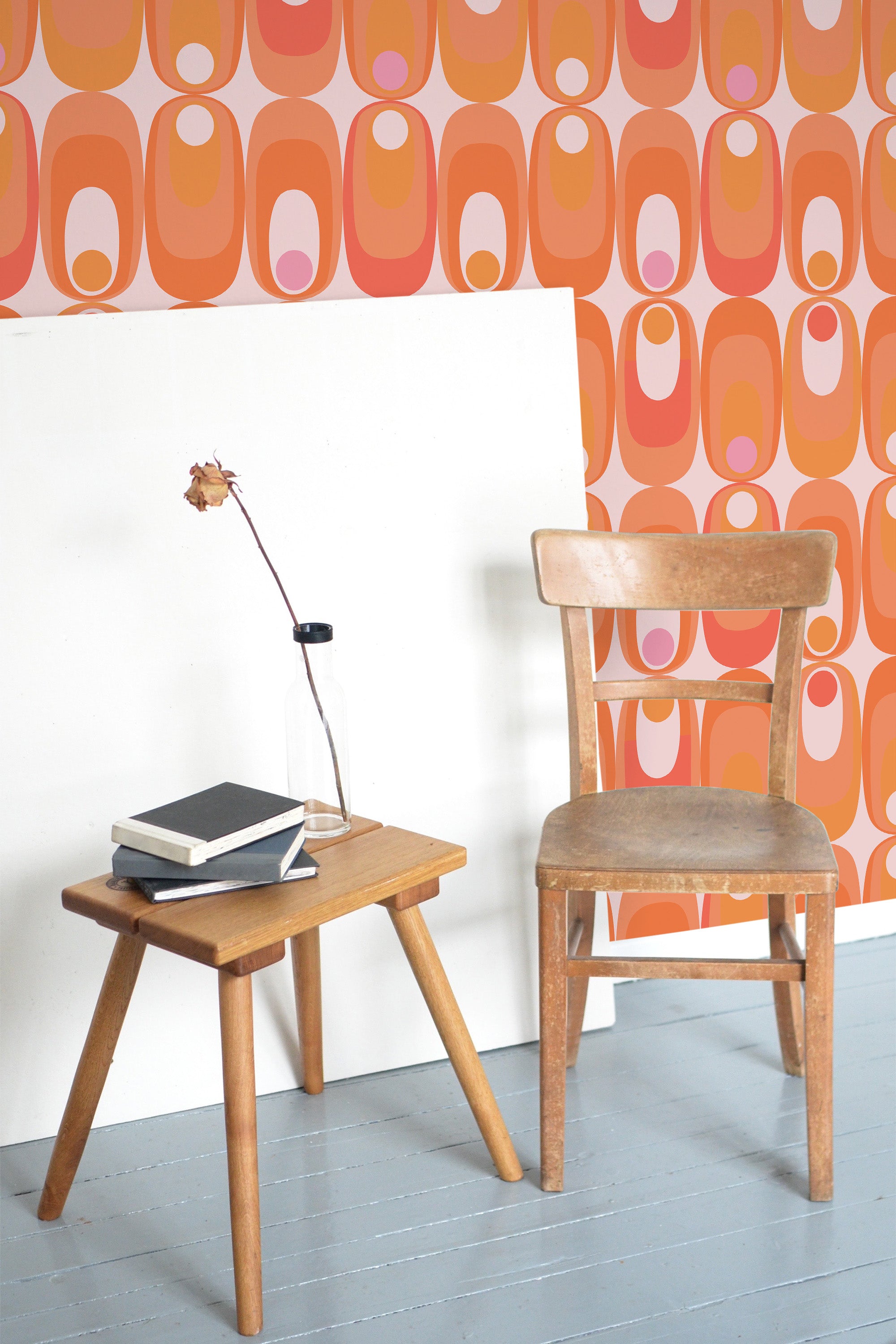 Self-adhesive orange retro circles wallpaper with overlapping geometric patterns on a wall, accompanied by a wooden chair and side table with books and a lamp.