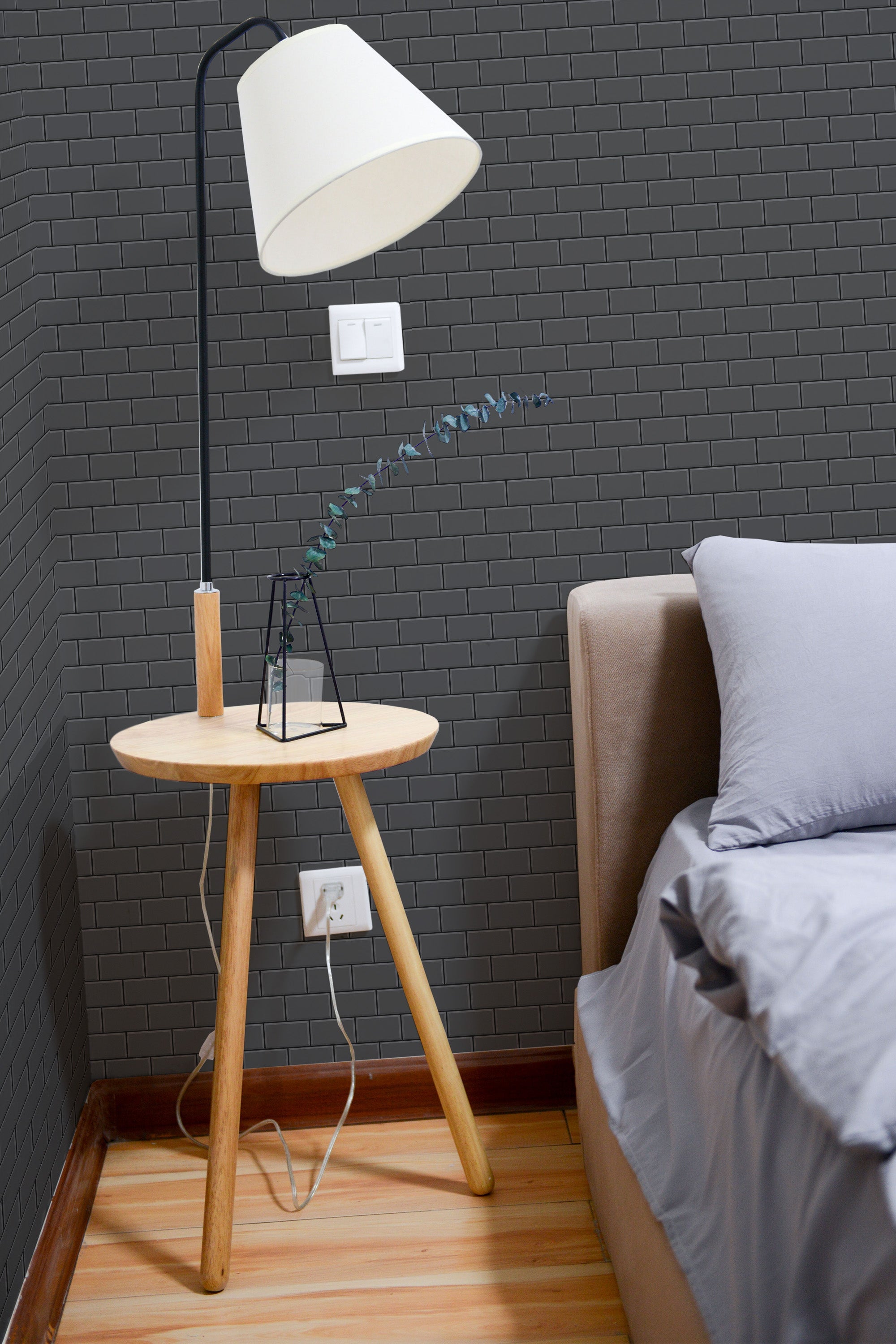 Self-adhesive gray brick design wallpaper on a bedroom wall with a floor lamp and a wooden bedside table.