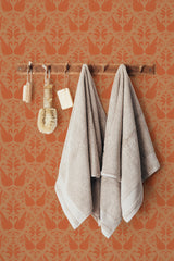 Self-adhesive wallpaper with an orange swan pattern on a wall, complemented by hanging soft towels and wooden bathroom accessories.
