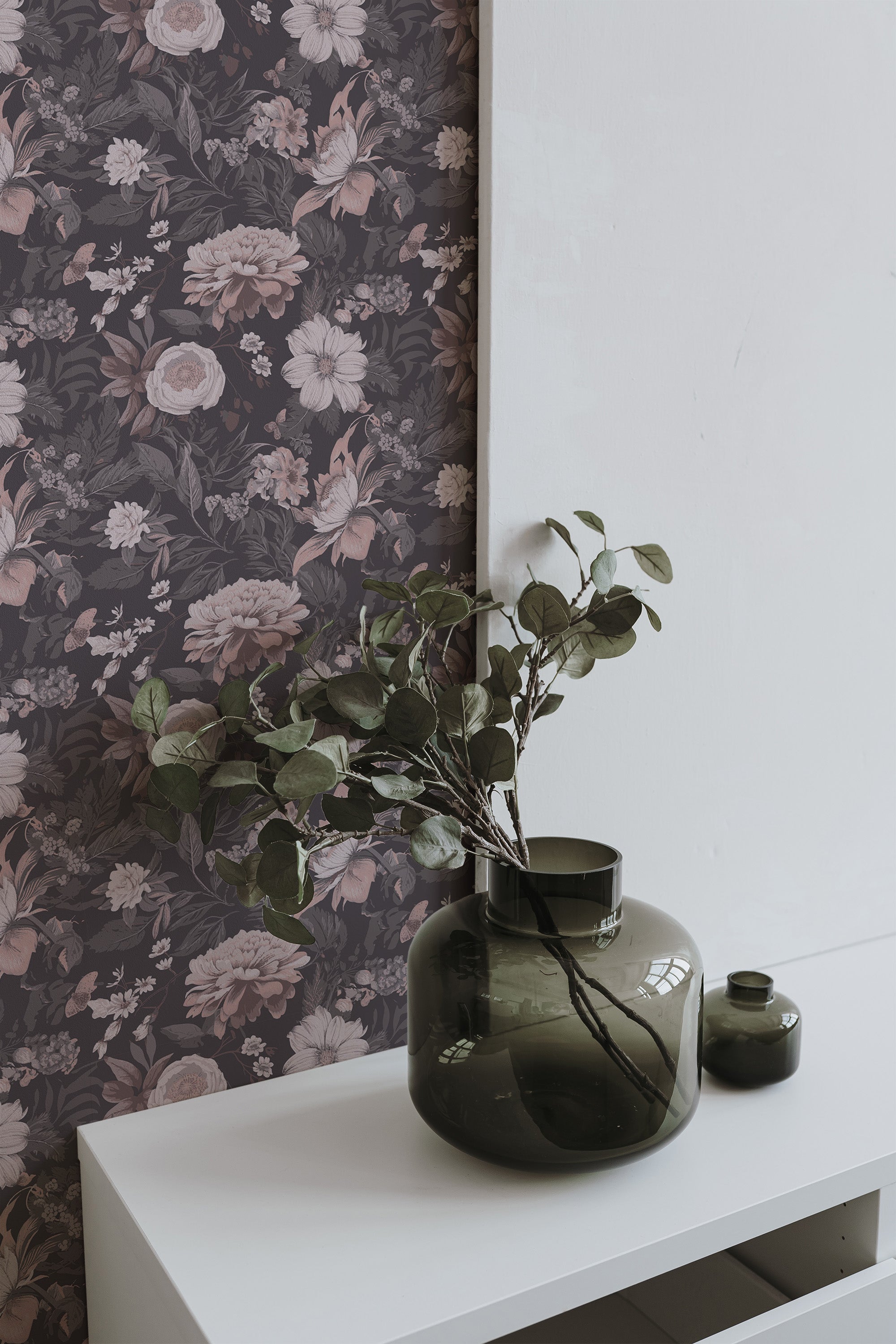 Self-adhesive Washed out floral wallpaper with muted pink and grey flowers on a dark background, complemented by green glass vases on a white shelf.