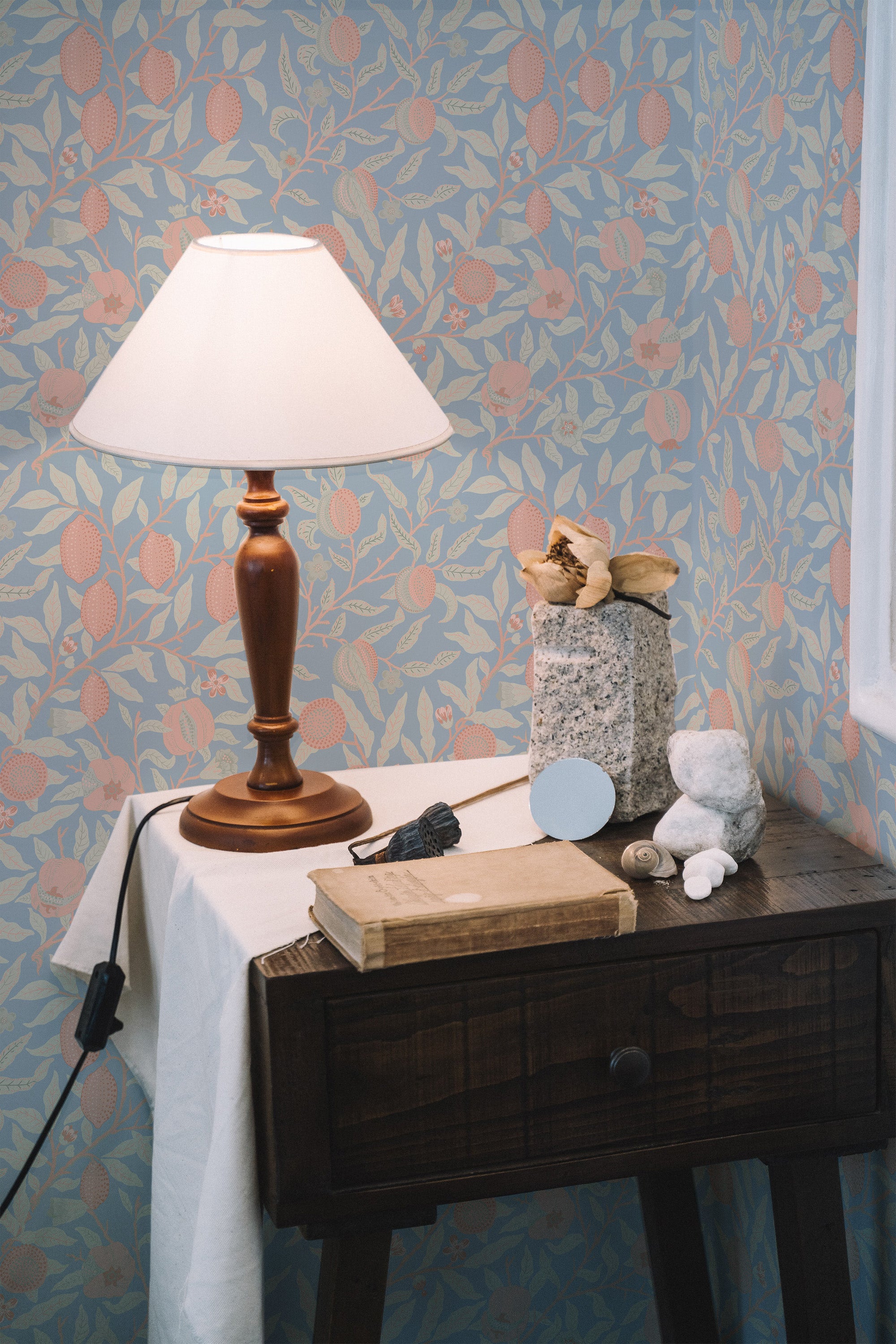 Self-adhesive wallpaper with lemon grove design, showing lemons and leaves in a repeating pattern on blue background, with a wooden side table and lamp in the foreground.