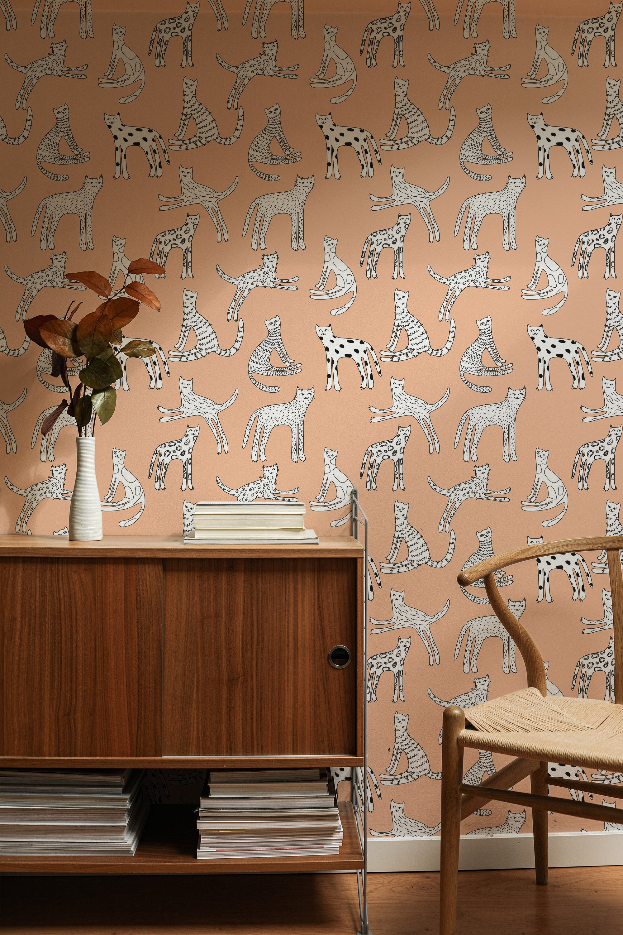 Self-adhesive wallpaper with cute cat illustrations in various playful poses on a warm background, behind wooden furniture.
