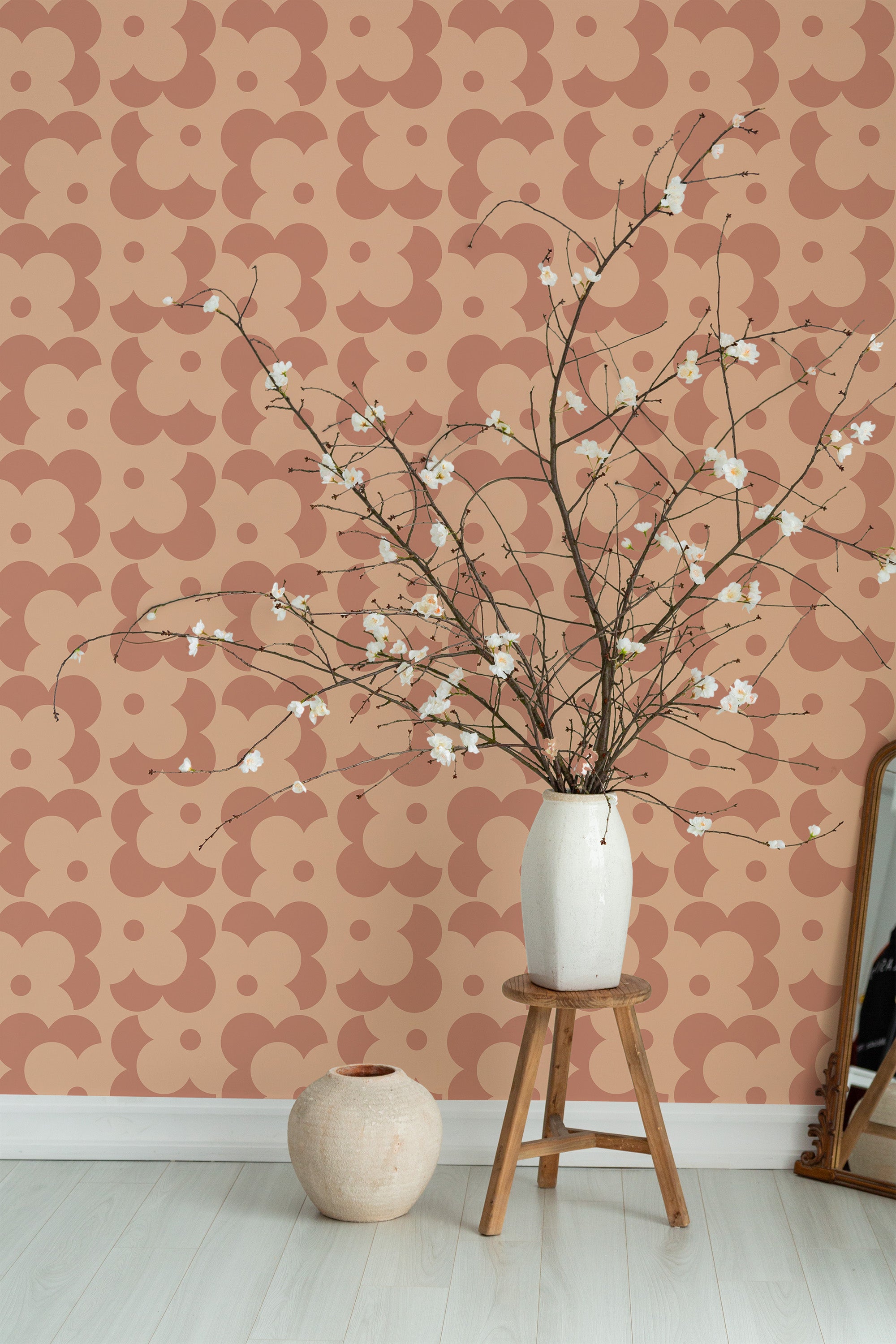 Self-adhesive wallpaper in a Peachy Simple Retro design with overlapping semicircle patterns in shades of peach and brown on a wall, accompanied by a vase with branches on a wooden stool.