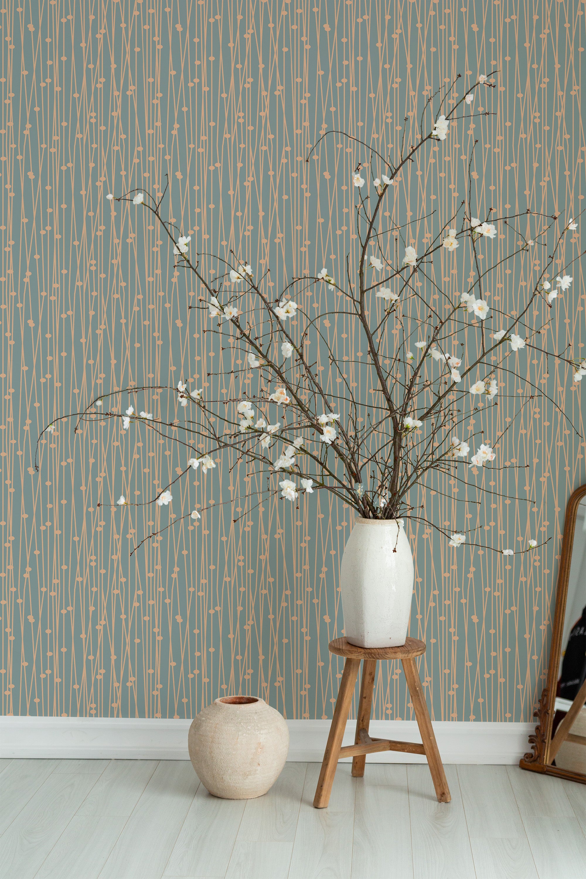 Self-adhesive wallpaper with geometric lines and peach accents in a modern room, complemented by a vase with branches on a wooden stool.