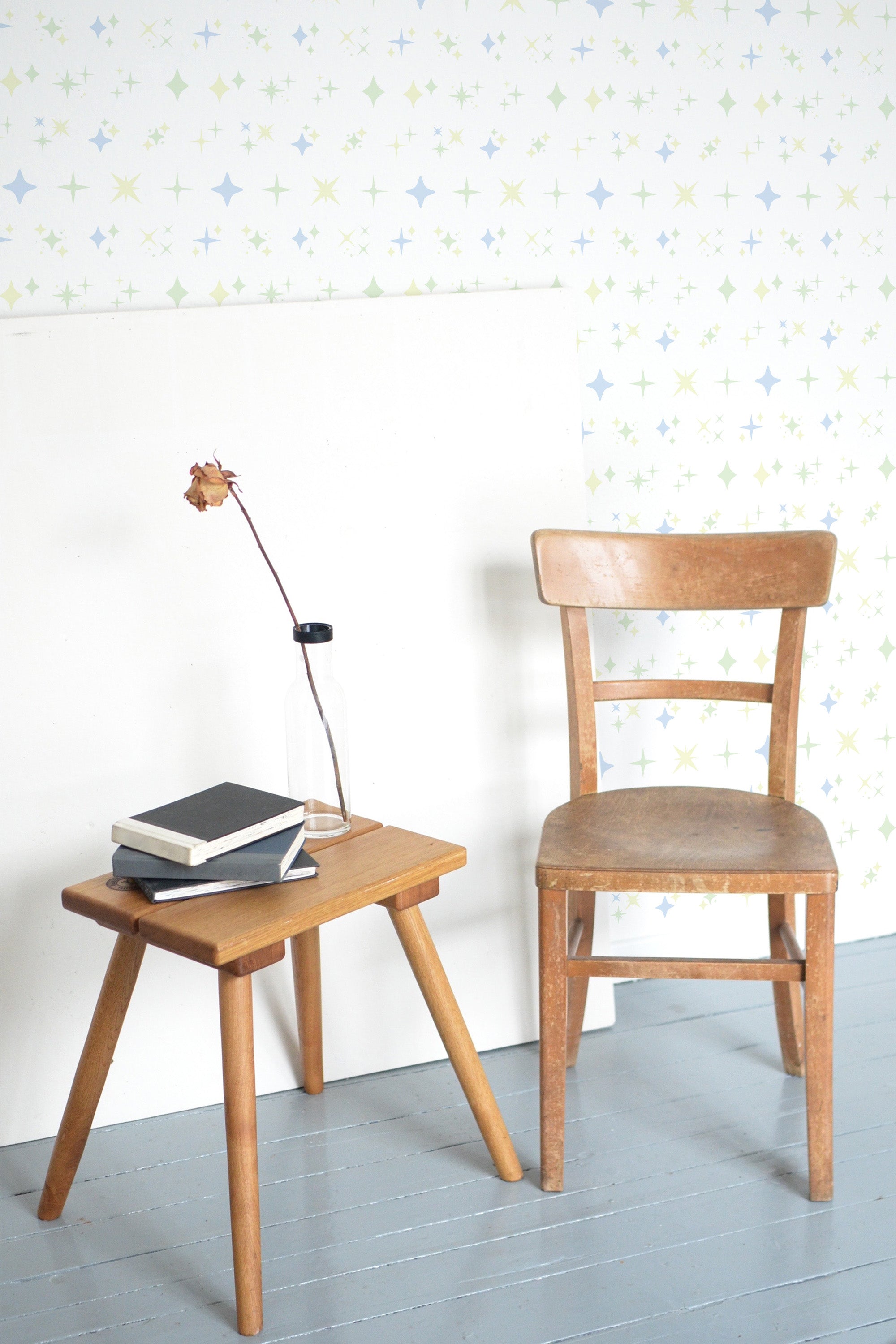 Self-adhesive wallpaper with a pattern of colorful stars on a white background in a room with a wooden chair and table.