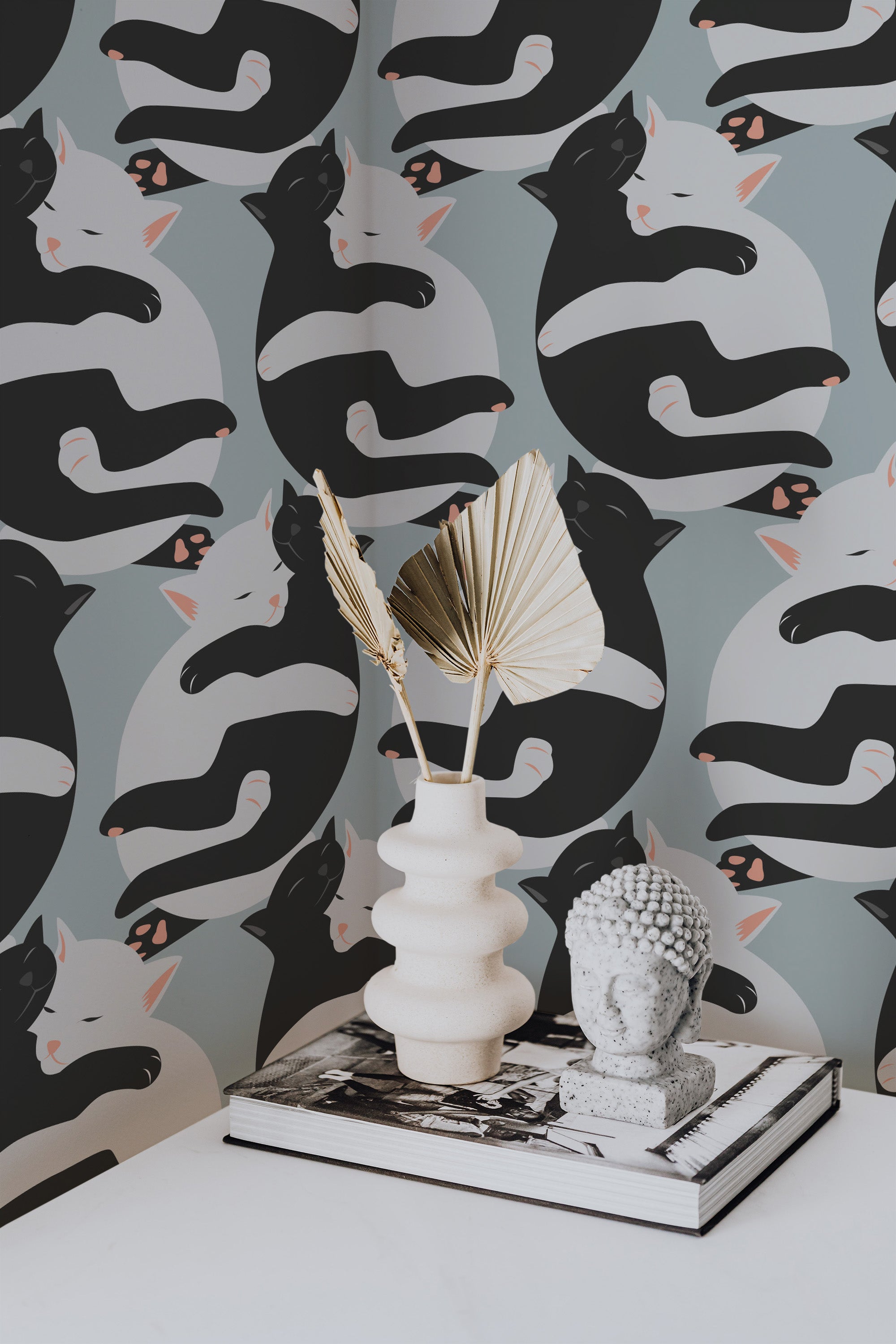 Self-adhesive wallpaper with a pattern of black and white kittens hugging on a gray background, accented by decorative items on a table.