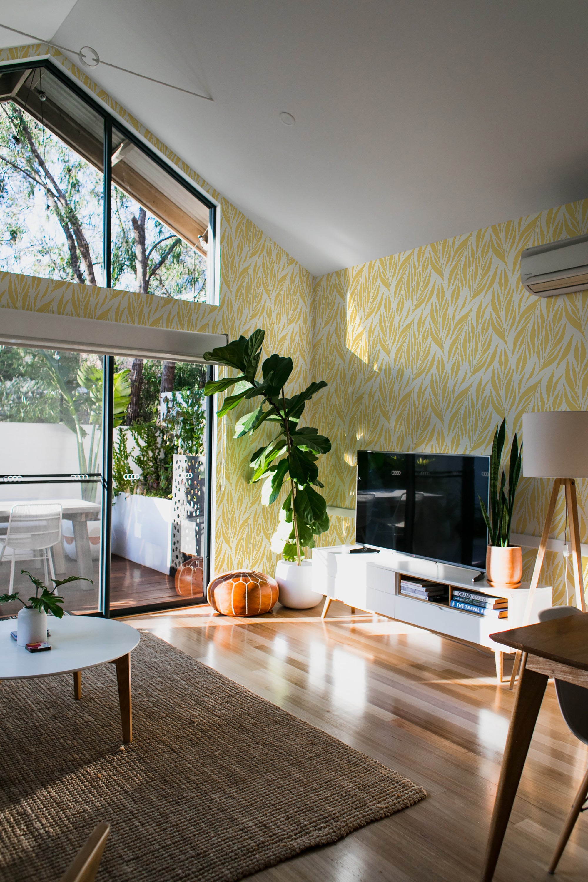 A room with yellow leaf-patterned wallpaper covering the wall, bringing a bright, nature-inspired design to a modern living space with large windows and wooden flooring. Traditional wallpaper.